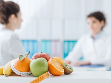 Two people sitting a table. There is a pile of fruit in front of them.